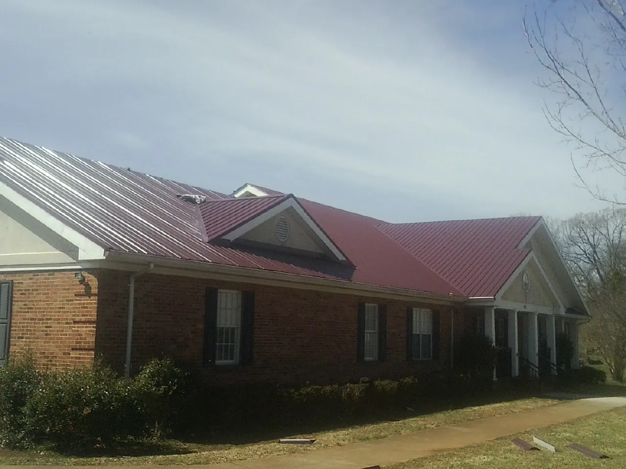 Red metal roof with gabled entries on a long brick building, from a Hail Damage Roof Repair job in Blaine